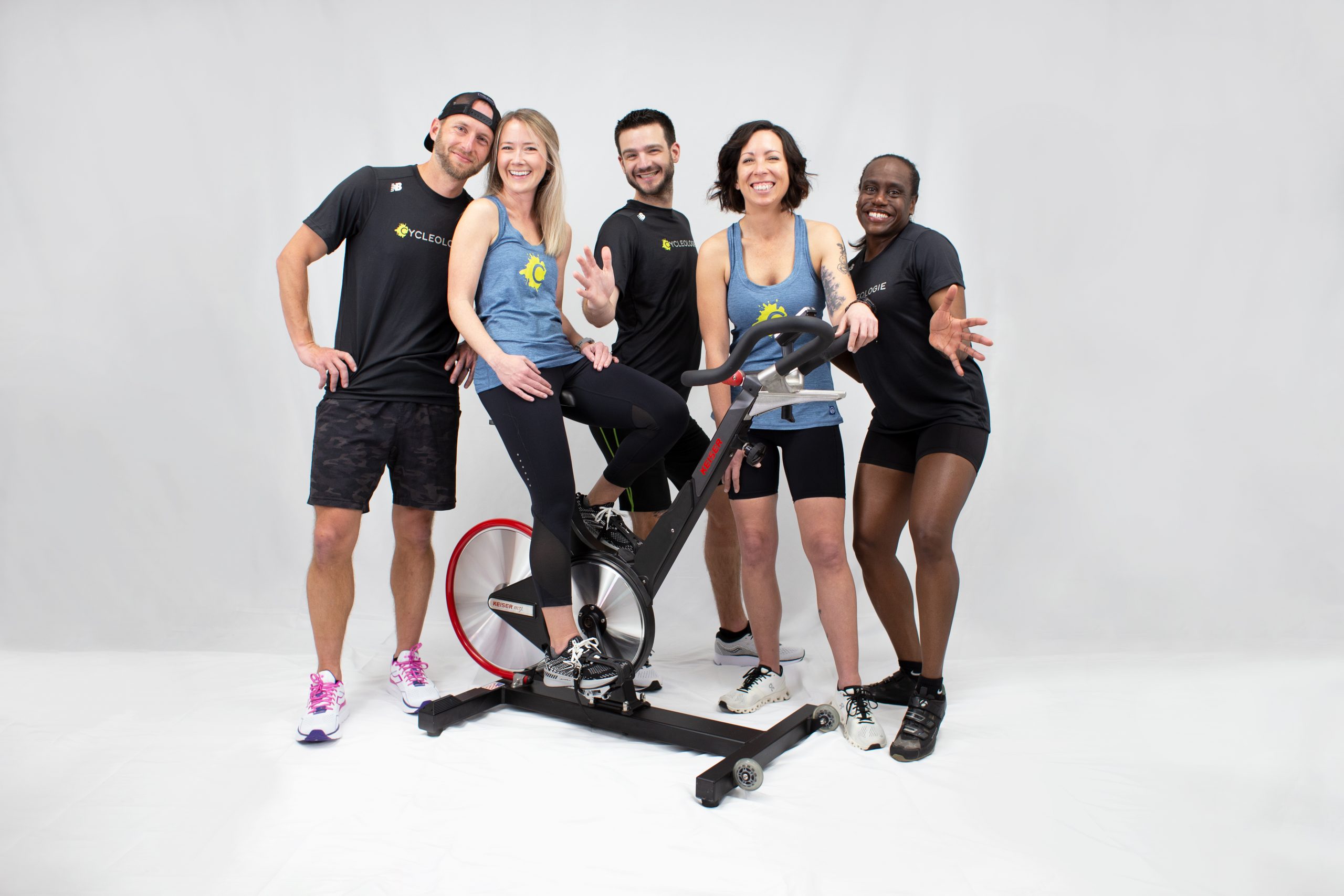 2 Men and 3 woman standing next to a stationary bike.